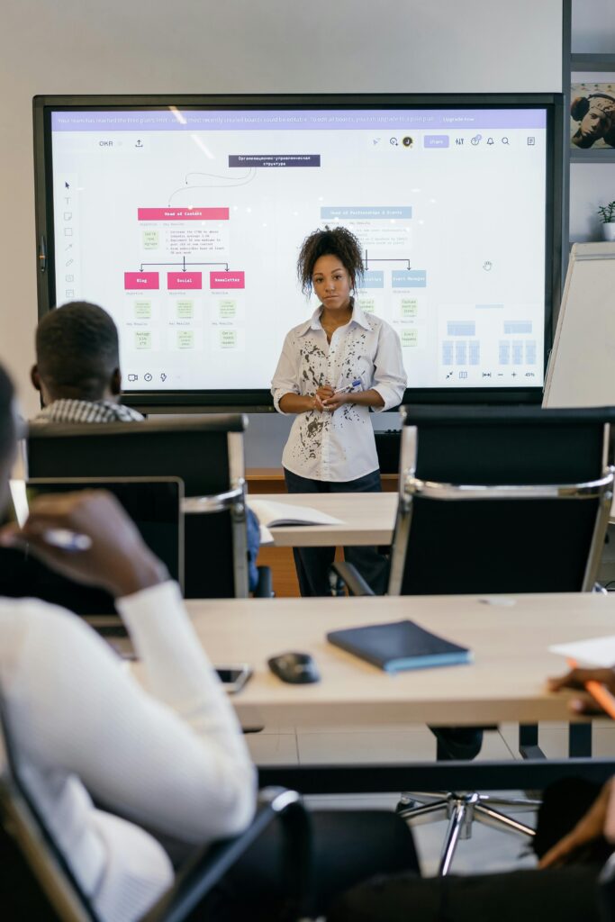 A professional business woman leads a meeting with a diverse team, using a digital display.